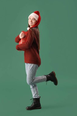 Noel Baba şapkalı genç bir kadın. Yeşil arka planda Noel hediyesi var.