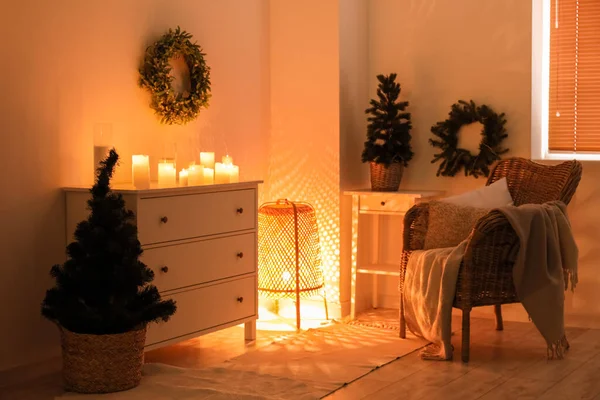 Interior of dark living room with Christmas wreaths, drawers and burning candles