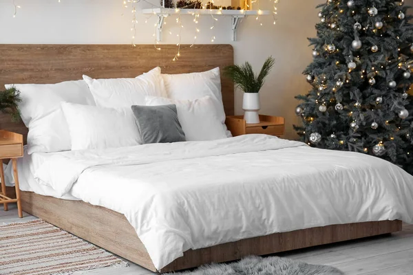 Interior of light bedroom with Christmas tree and glowing lights
