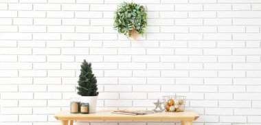 İçinde köknar ağacı, mum, Noel balosu, dergi ve ökseotu çelengi olan bir masa.