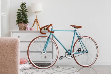 Oturma odasında Noel ağacı ve lamba olan çekmecelerin yanındaki bisiklet.