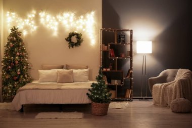 Yatak odasının içinde Noel ağaçları, çelenkler ve geceleri parlayan ışıklar var.