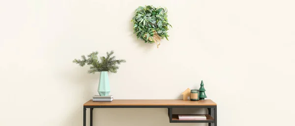 Table with fir branches in vase, Christmas decor and mistletoe wreath in light room