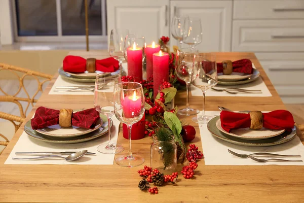 Christmas table setting with burning candles, fir cones and rowan in kitchen