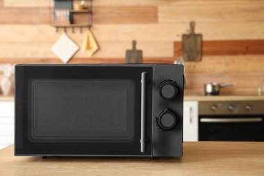 Mutfaktaki ahşap masada siyah mikrodalga fırın.