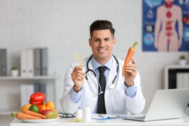 Male doctor with vitamins and vegetables sitting at table in clinic clipart