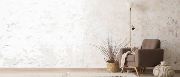 Stylish armchair, floor lamp, pouf and decor near light wall. Banner for design