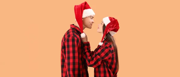 Happy Young Couple Santa Hats Checkered Pajamas Beige Background — Stock Photo, Image