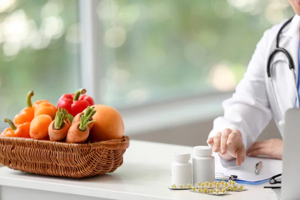 有维生素和蔬菜的女医生坐在诊所的桌子旁 — 图库照片