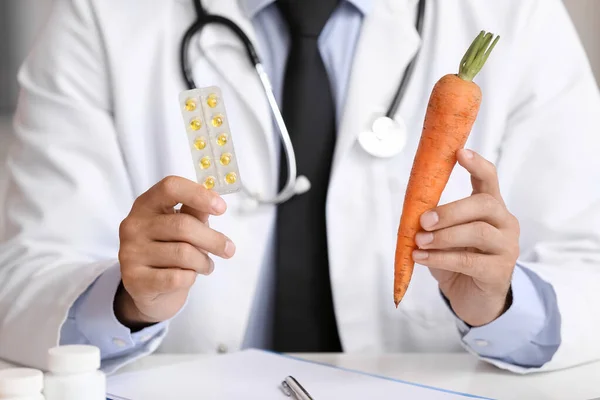 stock image Male doctor with vitamins and carrot in clinic, closeup