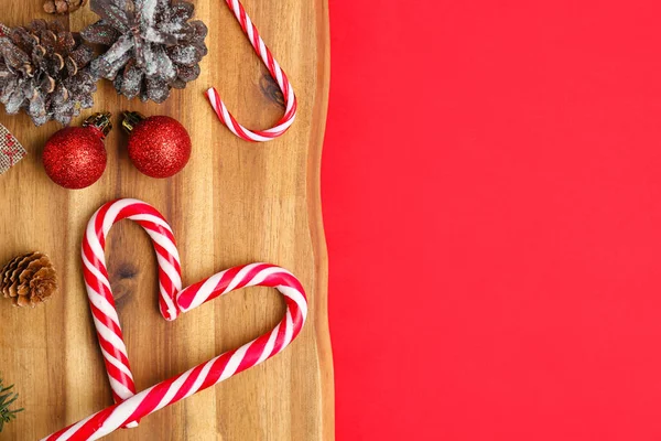 赤い背景においしいキャンディーの杖とクリスマスの装飾を持つ木製のボード — ストック写真