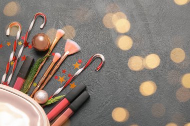 Makyaj malzemesi ve koyu arkaplan üzerine noel süslemeleri olan bir çanta.