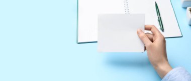 Boş kağıt, defter ve kalemle mavi zemin üzerinde yazı için boşluk olan kadın eli
