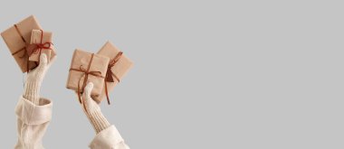 Gri zemin üzerinde Noel hediyesi kutuları tutan eller ve metin için boşluk