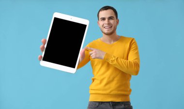 Açık mavi arka planda büyük tablet bilgisayarı olan yakışıklı bir genç.