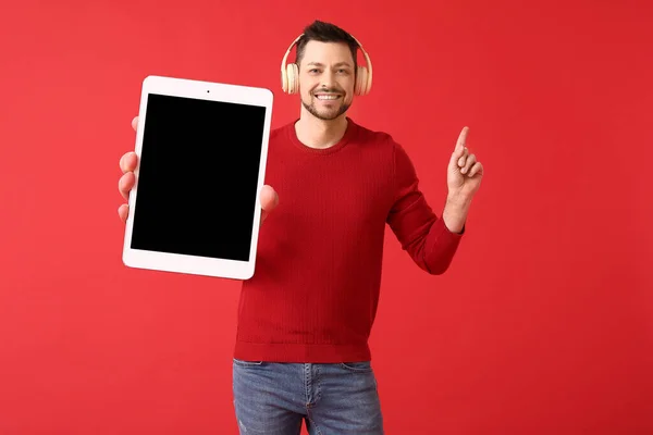 赤い背景に何かを指している大きなタブレットコンピュータとヘッドフォンを持つ男 — ストック写真