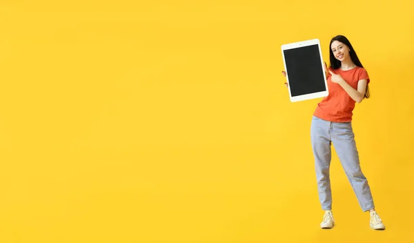 Junges Mädchen Zeigt Auf Großen Tablet Computer Auf Gelbem Hintergrund — Stockfoto