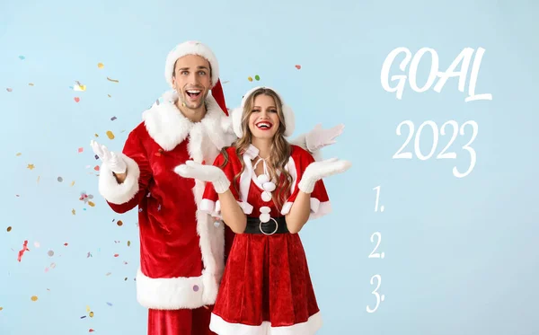 2023年 一对年轻夫妇穿着圣诞老人的衣服 穿着浅蓝色背景的空白待办事项清单 — 图库照片