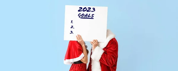 若いですカップルドレスとしてSanta Clauses Holding Blank List Year 2023のためにライトブルーの背景 — ストック写真