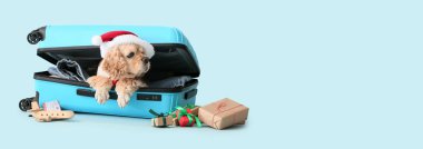 Noel Baba şapkalı ve bavullu sevimli köpek açık mavi arka planda ve mesaj için yeri var. Noel tatili konsepti
