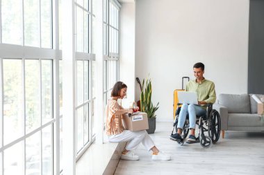 Taşınma gününde kocasıyla tekerlekli sandalyede eşyalarını toplayan genç bir kadın.