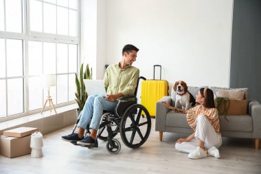 Kocasıyla tekerlekli sandalyede olan genç bir kadın ve taşınma gününde köpeği odada.