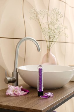 Lavabolu masa, seks oyuncakları ve bej duvarın yanındaki çiçekler.