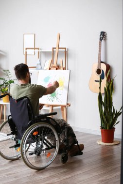 Tekerlekli sandalyedeki genç asker evde resim yapıyor.