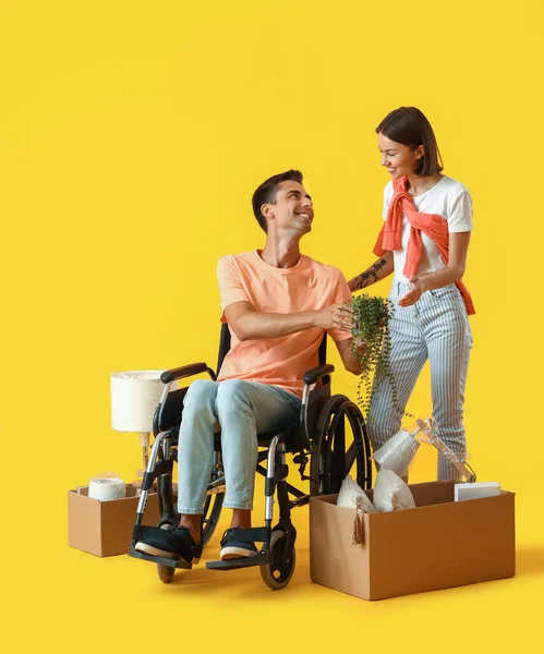 若いです女性とともに彼女の夫で車椅子と黄色の背景に移動ボックス — ストック写真