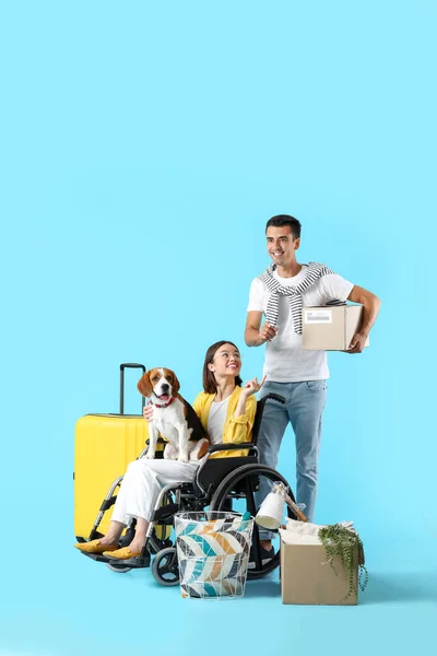 年轻男子 妻子坐在轮椅上 带着蓝色背景的移动箱子和狗 — 图库照片