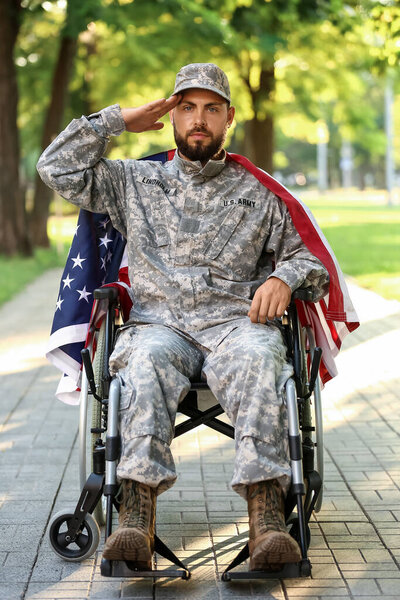 Young soldier in wheelchair with USA flag saluting outdoors