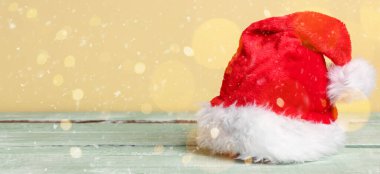 Noel Baba şapkası ahşap masada, sarı arka planda.