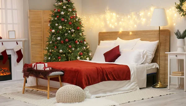 Interior of light bedroom with glowing lights and Christmas tree