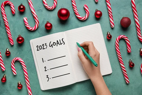 Woman making to-do list for year 2023 on green background, top view