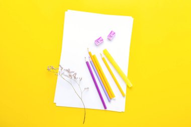 Kalemleri, keçeli kalemleri, kalemleri ve sarı arka planda çiçekleri olan boş kağıt kağıtlar.