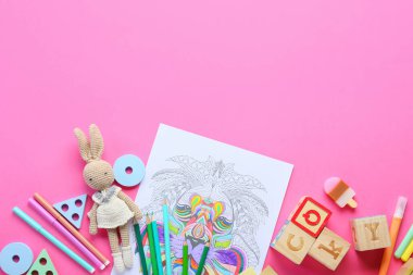 Boyama sayfası, keçeli kalemler, kalemler ve pembe arka planda oyuncaklar.