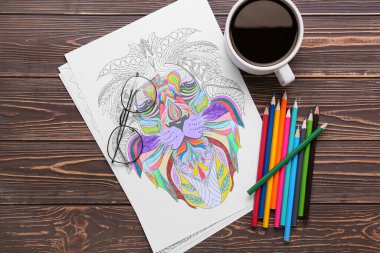 Boyama sayfası, gözlükler, kalemler ve koyu ahşap arka planda bir fincan kahve.