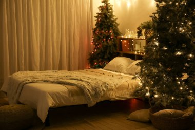 Karanlık yatak odasının içinde Noel ağaçları, raf ünitesi ve parlayan ışıklar var.