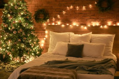 Karanlık yatak odasının içinde Noel ağacı ve parlak ışıklar var.