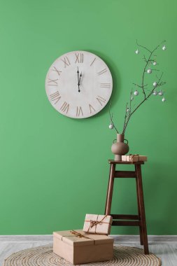 Ağaç dalları olan vazo, Noel baloları ve yeşil duvarın yanındaki masada hediye.