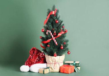 Noel Baba şapkalı küçük bir Noel ağacı ve yeşil arka planda hediyeler.