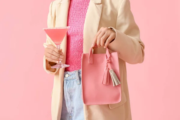 Woman holding pink lady cocktail and handbag on color background, closeup