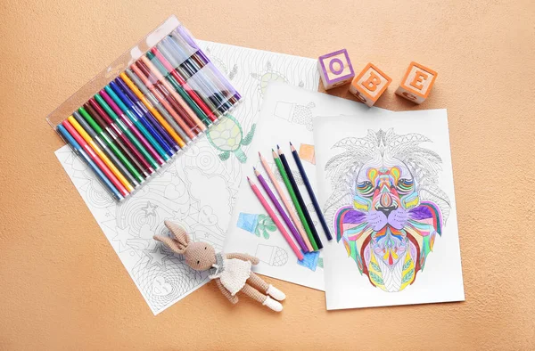 Coloring pages, felt-tip pens, pencils and toys on beige background