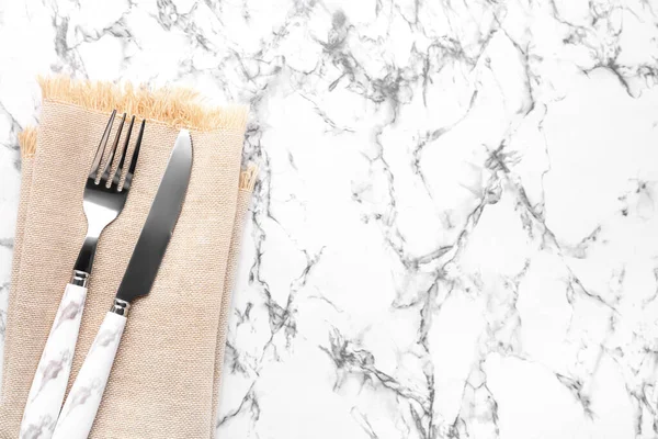 Silver cutlery with napkin on white marble background