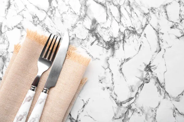 Silver cutlery with napkin on white marble background, closeup