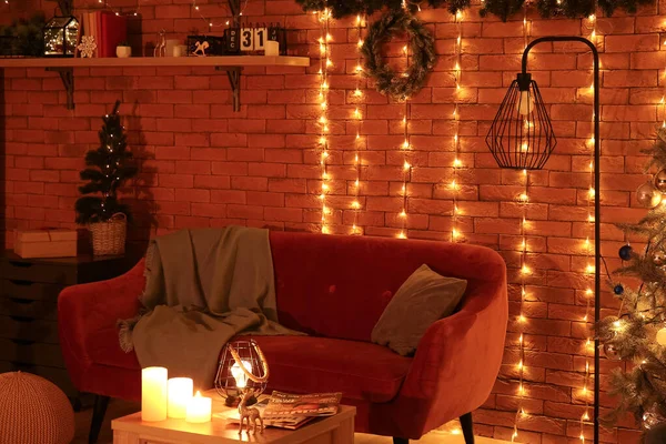 Interior of living room with Christmas wreath, sofa and glowing lights at night