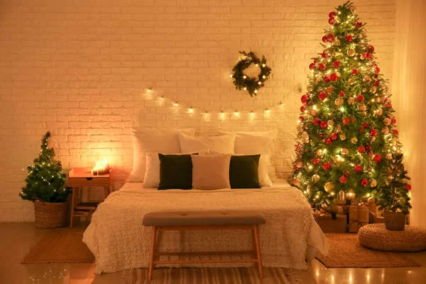 Interior of bedroom with Christmas trees, wreath and glowing lights at night