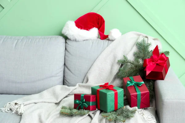 Καναπές Καπέλο Σάντα Χριστουγεννιάτικα Κλαδιά Και Δώρα Κοντά Πράσινο Τοίχο — Φωτογραφία Αρχείου