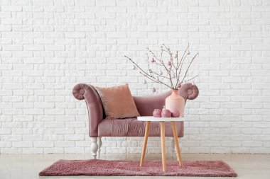 Ağaç dalları olan vazolar, masada noel topları ve beyaz tuğla duvarın yanında koltuk.