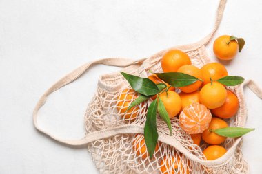 Olgun mandalinalarla dolu bir torba ve açık arkaplanda yapraklar.